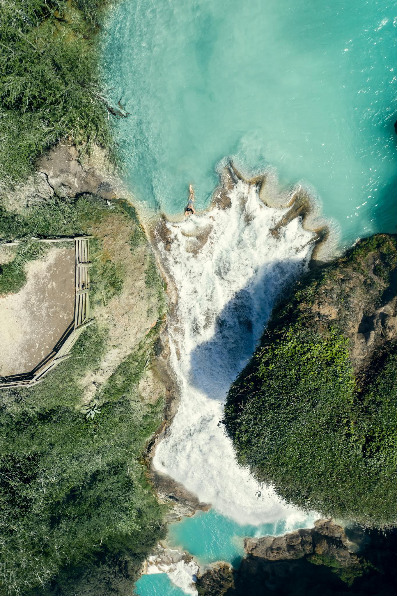 A stunning aerial shot capturing a waterfall cascading into a serene turquoise pool surrounded by lush greenery.